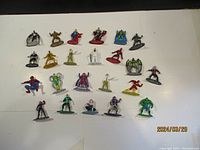 Photo showing 24 die cast metal figures from Marvel and DC comics arranged on a flat surface. Figures include popular characters in various poses.
