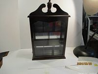 Front view of a dark wooden display case with glass door and decorative top finial.
