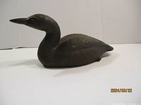 Side view showing full body profile of bronze loon sculpture on white background.