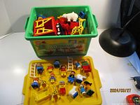 Full view of green bin filled with assorted LEGO DUPLO pieces including figures, animals, and building blocks on a yellow lid