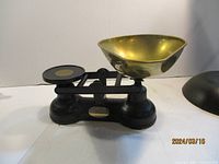 Side view of metal balance scale with black base and brass bowl.