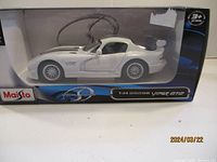 Front side view of white with blue striped Dodge Viper GT2 die cast model car in Maisto box showing detail and logo.