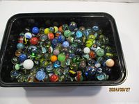 Black tray filled with over 100 assorted marbles in various colors and designs