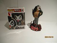Full view of KISS The Demon Funko Pop figure beside a bust statue of the same character on a white surface.
