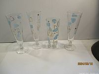 Front view of 4 retro glasses with abstract blue and gold markings, three tall and one shorter
