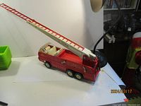 Side and top view of red metal Tonka fire truck toy with extended white ladder and white interior seats, placed on white background.