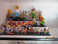 Wide view of 26 vintage cartoon and comic toy figures on shelves with various characters and colors.
