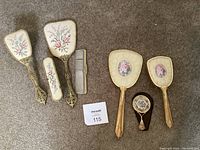 Two sets of vintage hair grooming items including hairbrushes, hand mirrors, combs, all with floral designs and gold-tone decorative elements.