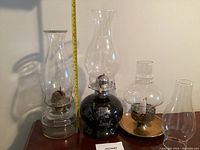 Three hurricane lamps: two oil lamps with chimneys and one brass candle holder with replacement glass chimney.