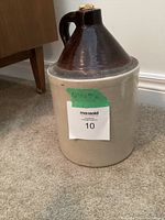 Photo of antique stoneware crock jug, showing beige bottom and dark brown top with handle and cork stopper.