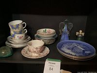 Shelf with two Grosvenor English China Windsor cups and saucers, one Rose Chintz Pink cup and saucer, stack of small plates, and two angel figurines