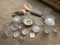 Overview of lot showing glass bowls, plates, candle holders, vase and 2 large conch shells.