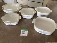 Photo of 5 white Corning Ware casserole dishes with blue floral cornflower design with 3 glass lids on countertop.