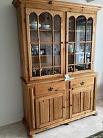 Front view of pine buffet and hutch showing closed glass paneled doors and wooden drawers and cabinet doors.