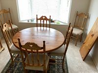 Full view dining table and six chairs in a tiled room with window light. Table circular shape and chairs arranged around.