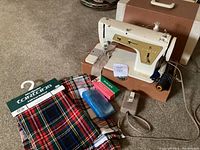 Singer sewing machine model 237, foot pedal, blue plastic case, and two tartan fabric remnants with tags, on carpet floor.
