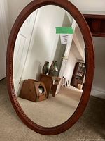 Front view showing oval wooden frame and clear mirror surface reflecting room interior.