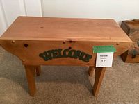 Front view of the small pine side table showing wood grain, natural finish, and 'WELCOME' green sign on the front