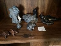 Soapstone animal carvings of a grey squirrel, loon, seal, chipmunk, penguin, and bear arranged on a wooden shelf.