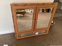 Front view of a solid wood vanity cabinet with two mirrored doors and a decorative panel below
