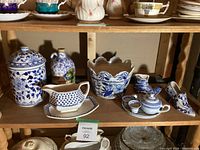 Shelf containing an assortment of blue and white ceramic and porcelain items including a canister, gravy boat, planter, boots, and jug.