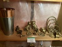 Overview of lot contents including two brass cats, a candle snuffer, letter opener, metal cup, and brass letter holder on wooden shelf.