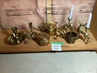 Overview of lot showing all brass items on wooden surface with maxsold lot tag 104.
