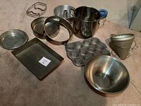 Photo showing collection of vintage metal baking pans and kitchen utensils including baking pans, muffin pan, metal bowl, colander/strainer, and soup pot