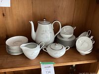 Full tea set arranged on a wooden shelf including teapot, creamer, sugar bowl, cups with saucers, and small plates.