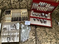 Three vintage silverware sets in original boxes showing knives, forks, spoons and serving utensils on floral upholstered background