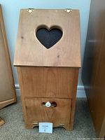 Front view of the closed wooden potato and onion box showing heart-shaped cutout and white knob on bottom door.