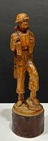 Front view of the detailed wooden statue showing soldier with helmet, bag, and equipment on a round base.