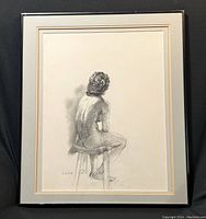 Full view of framed charcoal drawing of nude figure seated on stool, showing entire artwork with matting and frame.