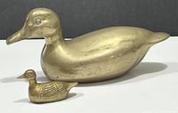 Side view of large vintage brass duck doorstop with smaller brass duck paperweight in front showing size scale and details