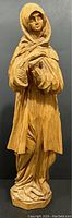 Full view of the wood carved statue showing height, overall shape and folds of cloak