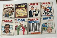 Top-down view of all 8 MAD magazines laid flat showing front covers with colorful 1970s style satirical artwork