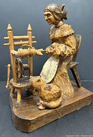 Front and side view of hand carved wood sculpture of a woman spinning wool on a spinning wheel with a cat at her feet.
