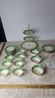 Tea set including cups, saucers, soup cups, plates, and 3-tier pastry stand all with green and gold trim on bone china