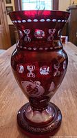 Front view of burgundy glass vase highlighting overall shape and cut glass decoration with white motifs on red glass.