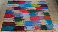 Full view of colorful hooked rug with patchwork of colors and irregular rectangular designs in blue, red, green, brown, and beige tones.