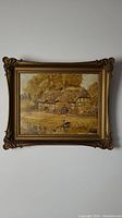 Framed oil painting showing the full artwork of a rural thatched cottage scene with a small pond and feeding ducks.