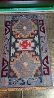 Full view of handmade hooked rug showing Aztec design and wooden dowel for hanging