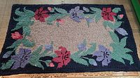 Full view of rectangular hooked rug showing floral pattern with red and purple flowers on dark blue border and beige center, placed on floor with measuring tape showing 39 inches length