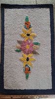 Full view of hooked rug showing central floral design and dark border