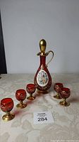 Full set of Italian red glass decanter with five matching small glasses on a light tablecloth.