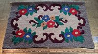 Full view of hooked rug laid flat showing floral design and wooden dowel