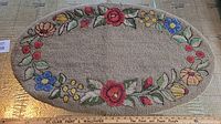 Full view of oval hooked mat showing beige background and multicolored floral border
