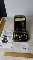 Front view of the black Pac-Man tabletop arcade game unit with colorful character decals and original instruction manual.