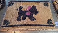 Full view of the rectangular hooked mat with black Scottish dog and floral corners on beige background
