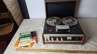 Full view of Sony Stereo Center 230 reel to reel tape recorder with two reels loaded, and stack of extra tapes and booklets beside it.